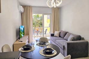 Habitación de hotel con comedor, sofá y balcón con vistas a zonas verdes.