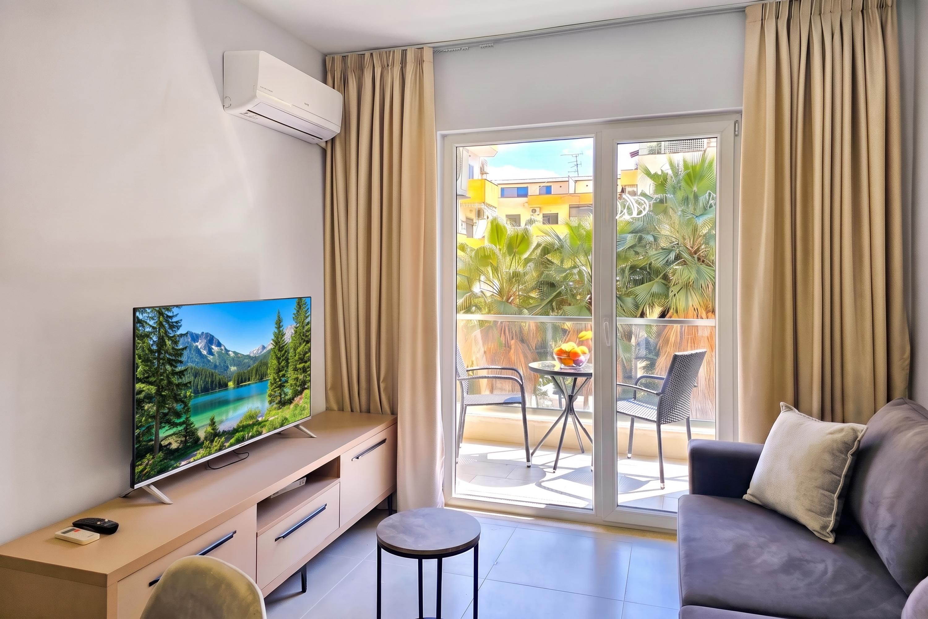 Een moderne woonkamer met een flatscreen televisie, een bank, een salontafel en een balkon met uitzicht op een meer en bergen.