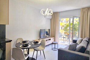 A modern living room with a dining area, a flat-screen TV, and a balcony with a view of the city. - Happy Stay Apartment By The Sea 092, Durres, Albania (Durres)