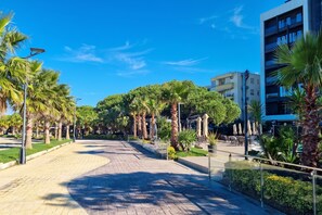 A paved walkway lined with palm trees and a modern building with balconies. - Sea View Holiday Apartment 073, Durres, Albania (Durres)