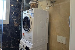 Eine gestapelte Waschmaschine und ein Trockner in einem Badezimmer mit Marmorwand und einem darauf stehenden Korb mit dem Aufdruck 'Smart Home'.