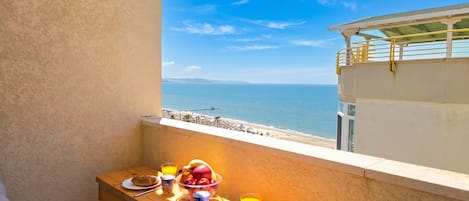 A balcony with a breakfast setup overlooking a beach and the sea.
