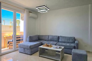 A modern living room with a grey sectional sofa, a glass coffee table, and a ceiling light fixture. - Sea View Holiday Apartment 073, Durres, Albania (Durres)