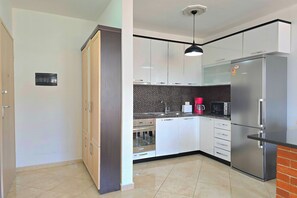 Eine moderne Küche mit weißen Schränken, einem Edelstahl-Kühlschrank, einer Mikrowelle und einer Kaffeemaschine.