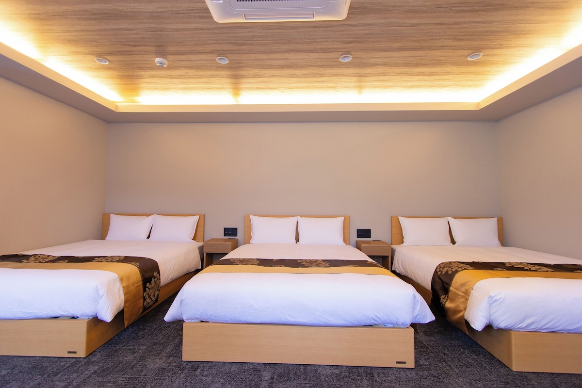 A hotel room with three single beds, wooden headboards, and a ceiling with recessed lighting.