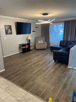 A modern living room with a flat-screen TV, a sofa, a chair, and a coffee table. - Green Aurora: 3 bed, 2 bath,  Laundry, King Bed (Fairbanks)
