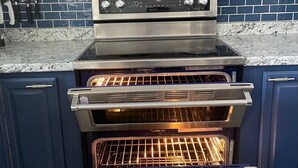 Een keuken met een inbouwoven, een magnetron en een betegelde spatwand.