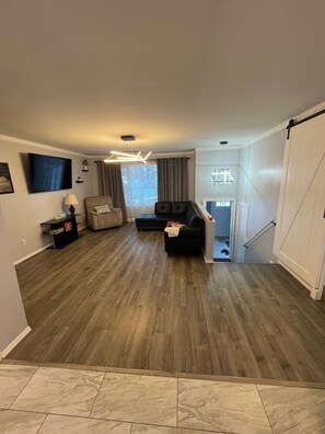 Ein Wohnzimmer mit einem Ecksofa, einem kleinen Tisch und einem Fernseher.