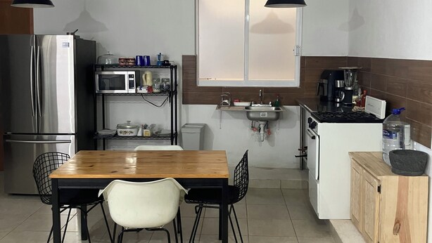 Cocina compacta con mesa, sillas, refrigerador, microondas, lavamanos y estufa.