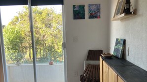 Una habitación con una cama, un escritorio de madera, una silla, una mesita con un cuenco y un ventanal corredero que da a un balcón.