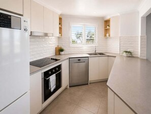 Eine moderne Küche mit weißen Schränken, einem Geschirrspüler, einem Backofen und einem Fenster mit Jalousien.