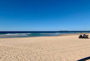 Ein Strand mit einem Golfwagen im Sand, blauem Himmel und dem Meer im Hintergrund.