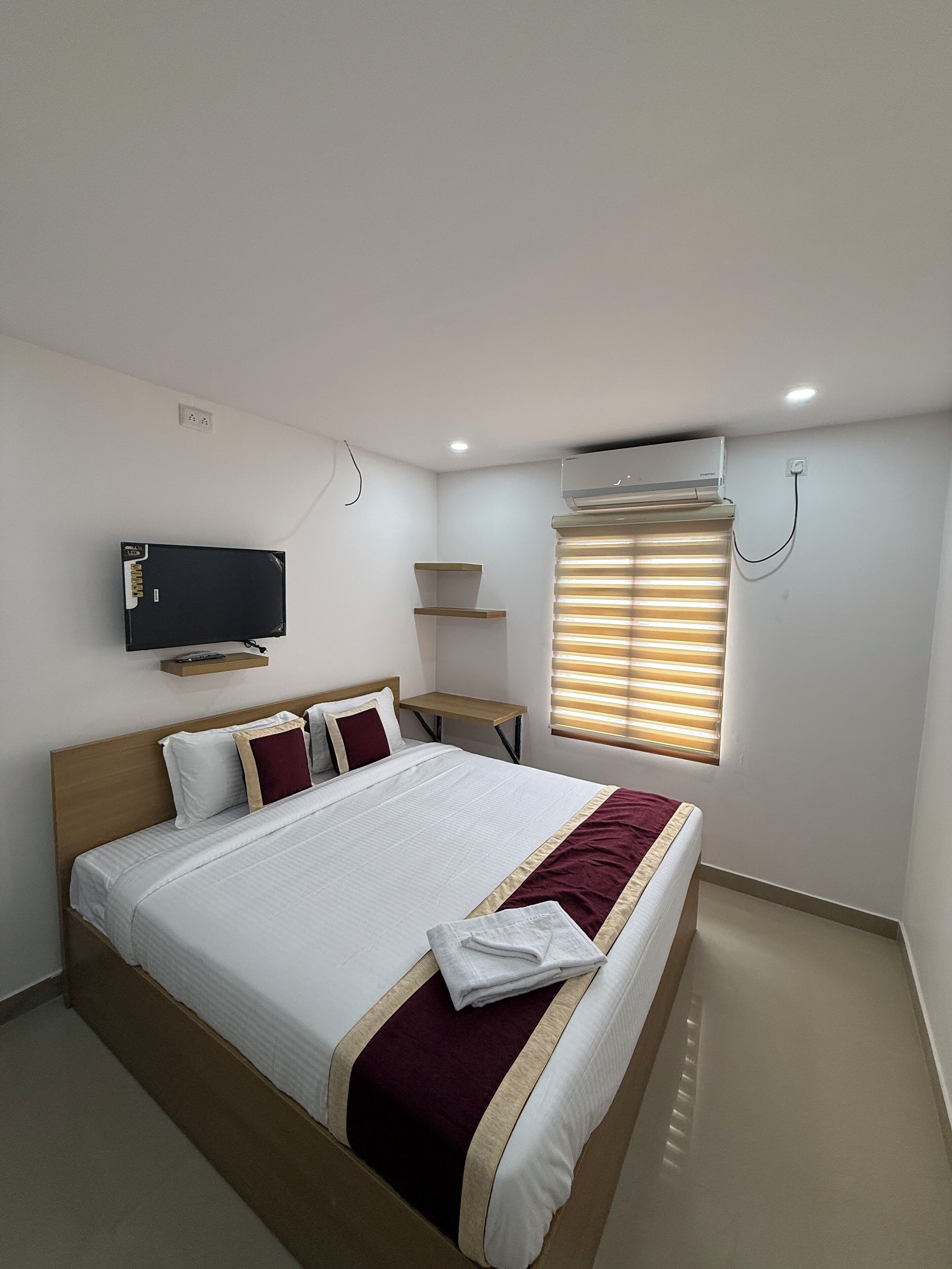 Een hotelkamer met een bed, een aan de muur bevestigde televisie, een airconditioning en een raam met zonwering.