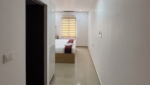 Een hotelkamer met een bed, een raam met luxaflex, een deur en een klein tafeltje.