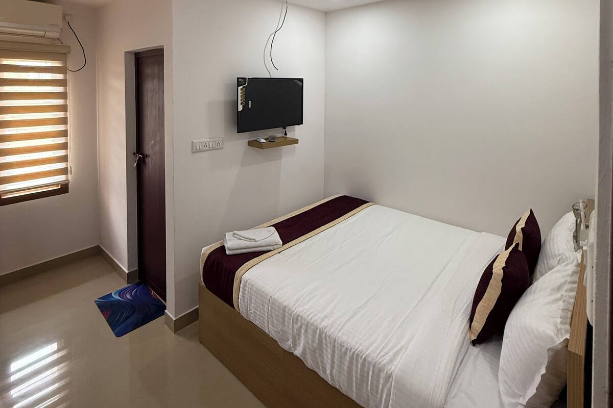 A bedroom with a bed, a TV mounted on the wall, and a door.