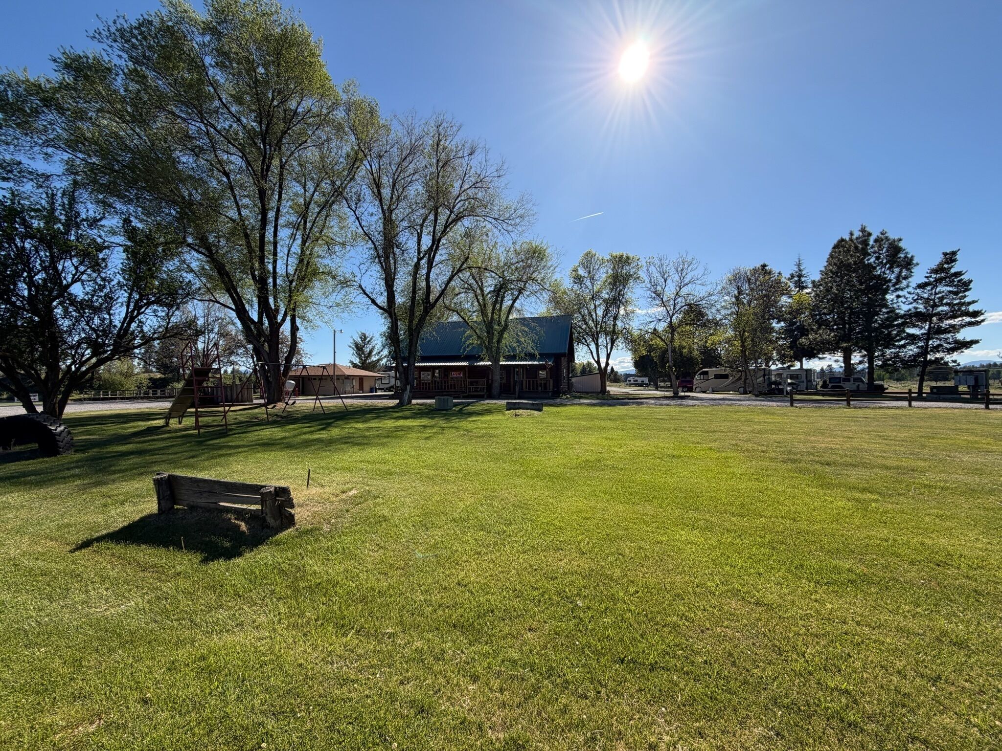 A grassy park area with trees, a playground, and a building with a blue roof.