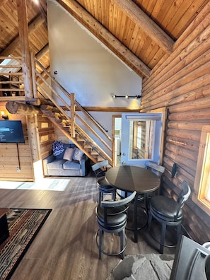 A log cabin interior with a dining area, sofa, staircase, and a TV. - The Waterwheel Cabin & Guide Room/Family Retreat (Chiloquin)