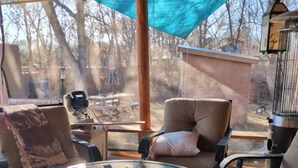 Une table ronde avec un plateau de nourriture, une chaise avec un coussin et une vue sur les arbres par la fenêtre.