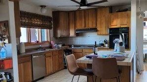 Une cuisine avec des meubles de rangement en bois, un ventilateur de plafond, un lave-vaisselle et un coin repas avec deux chaises.