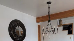 Une salle à manger avec une table en bois, des chaises à motifs, un lustre et un miroir au mur.