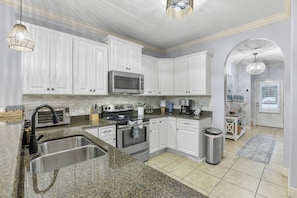 A modern kitchen with white cabinets, stainless steel appliances, granite countertops, and a visible trash can. - Navarre Sound Place (Navarre)