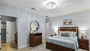 Une chambre à coucher avec un grand lit, une commode en bois, un miroir rond, une table de chevet et un lustre.