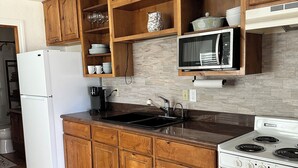 Una cocina con armarios de madera, un refrigerador blanco, una estufa, un microondas y un salpicadero de azulejos.