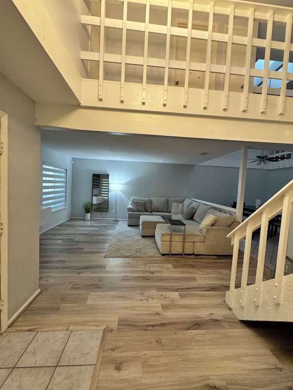 A spacious living area with a wooden floor, a large sectional sofa, and a staircase leading to an upper level. - Spacious & Clean Home for 6 – Small Patio & Garage (Houston)