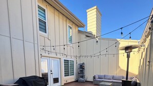 Un jardin avec une pelouse artificielle, une terrasse en bois, du mobilier d’extérieur et des guirlandes lumineuses.