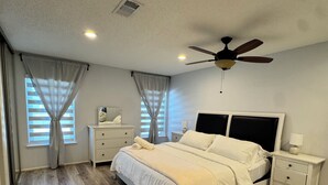 Une chambre à coucher avec un lit, des tables de chevet, un ventilateur de plafond et une fenêtre avec des rideaux.