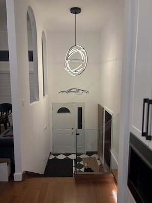 Un pasillo con una puerta blanca, un tapete blanco y negro, piso de madera y una lámpara en el techo.
