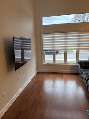 Una habitación con un ventanal grande, un televisor montado y suelo de madera.