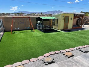 A backyard with artificial grass, a swing set, a fenced play area, and a small shed.