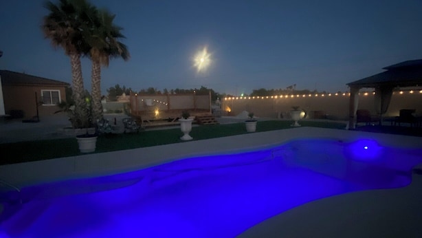 Une piscine éclairée de lumières bleues, avec des palmiers et des guirlandes lumineuses en arrière-plan.