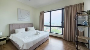 A hotel room with a large bed, a view of the city through a window, and a built-in ironing station. - Cozy 2BR Melaka Apartment, 5min Drive to Jonker St (Malacca City)
