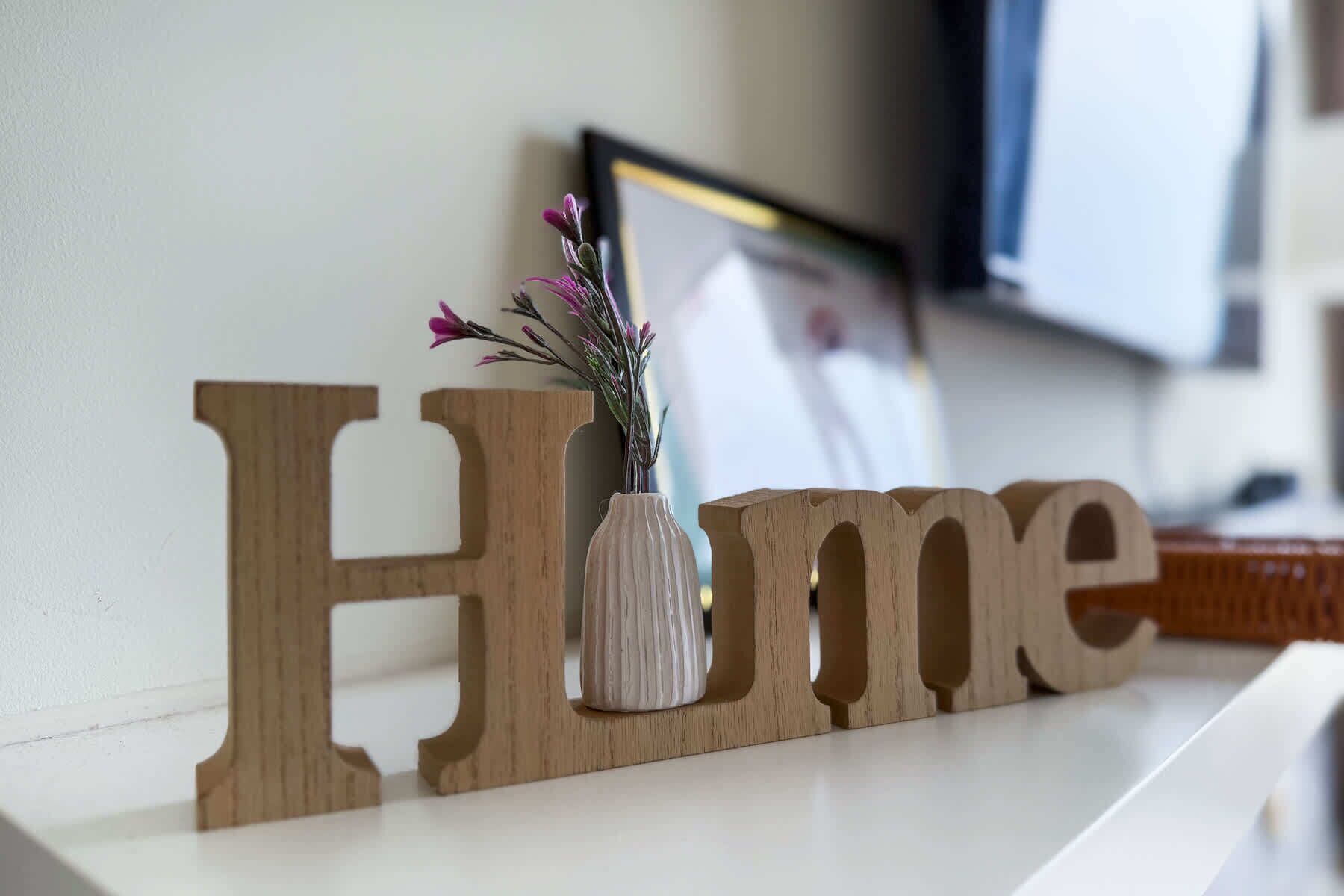 Wooden letters spelling "Home" on a white shelf with a vase of flowers.