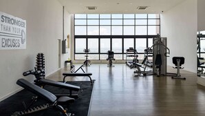 Ein Fitnessraum mit Trainingsgeräten, großen Fenstern und einem motivierenden Plakat.