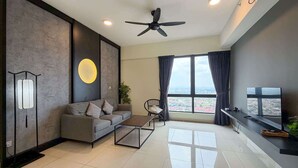 Ein modernes Wohnzimmer mit grauem Sofa, Couchtisch, Fernseher und einem großen Fenster mit Vorhängen.