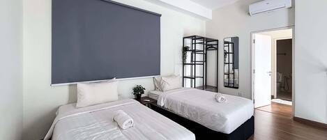 A modern hotel room with two beds, a ceiling fan, an air conditioning unit, and a large mirror.