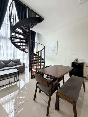 Un salon moderne avec un escalier en colimaçon, un canapé, une table à manger avec des chaises et un petit meuble noir.