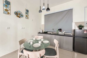 Una cocina moderna con zona de comedor, que incluye una mesa redonda de vidrio, sillas e iluminación colgante.