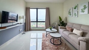 A modern living room with a flat-screen TV, a sofa, a coffee table, a ceiling fan, and a large window with curtains. - 2BR Melaka City Apartment, 5min Drive to Jonker St (Malacca City)