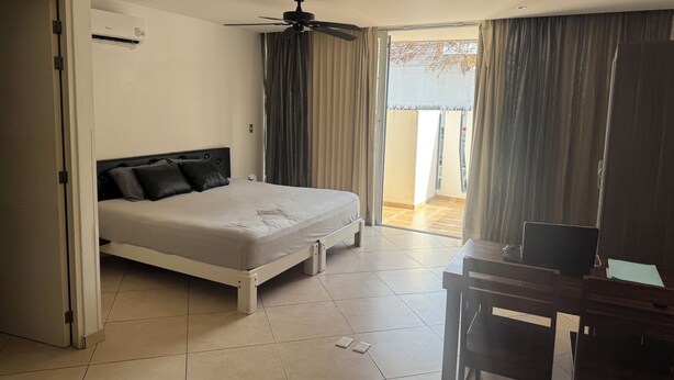 Ein Hotelzimmer mit Bett, Schreibtisch, Deckenventilator und Blick ins Freie.