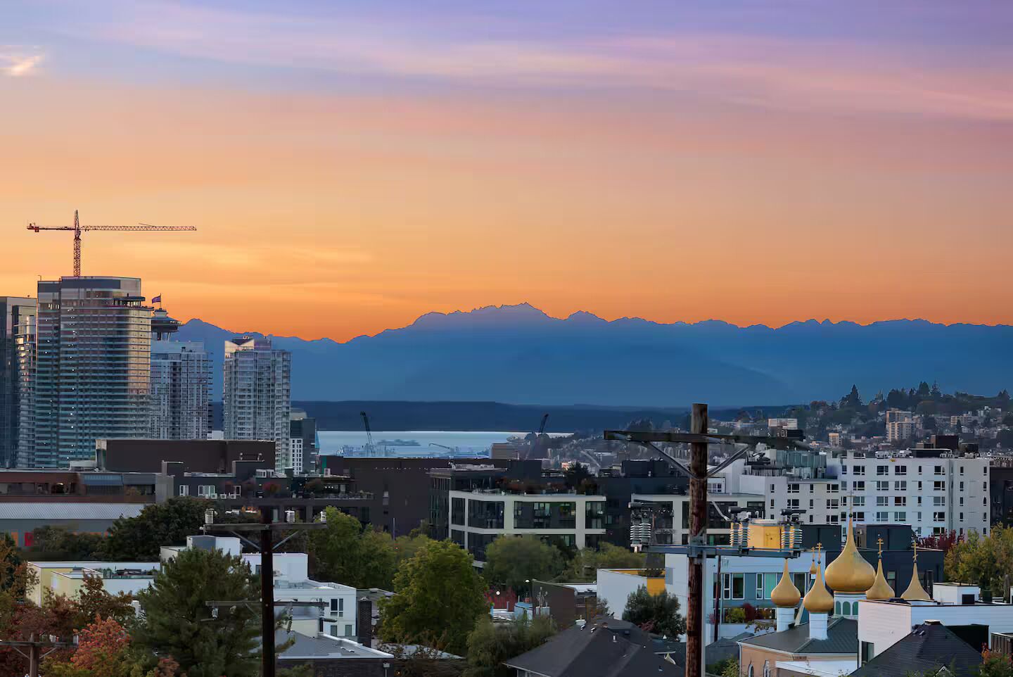 Une vue urbaine avec des bâtiments modernes, une grue de construction et une chaîne de montagnes en arrière-plan.
