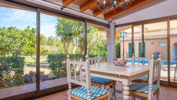 Uma sala de jantar com mesa e cadeiras, janelas amplas e vista para o verde lá fora.