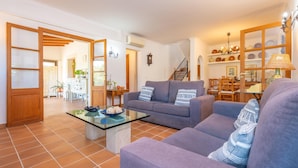 Uma sala de estar ampla com um sofá cinza, uma mesa de centro de vidro e uma área de jantar ao fundo.