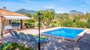 Piscina com espreguiçadeiras, área de estar coberta e montanhas ao fundo.