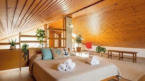 Ein gemütliches Zimmer mit Holzbalkendecke, einem Bett mit aufgerollten Handtüchern, einer Bank und Topfpflanzen.