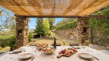 An outdoor dining area with stone pillars, a table set with plates, glasses, and a variety of food.