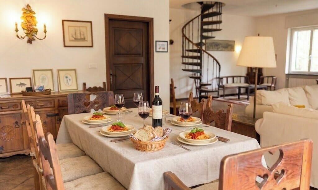 A dining area with a table set for a meal, chairs, a chandelier, a staircase, and a sofa.